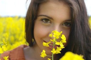 菜の花畑で菜の花1つを顔に近づけて笑顔を見せる女性
